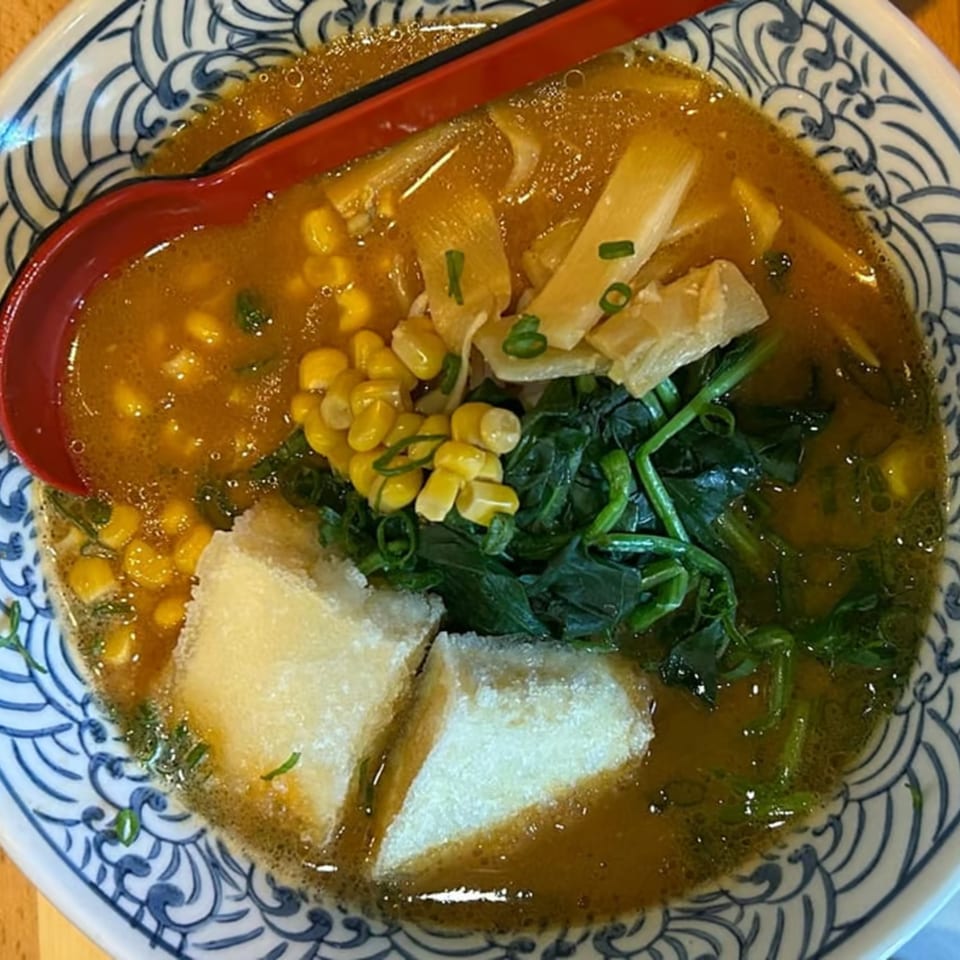 A bowl of Ramen Thukpa ramen with corn, spinach, bamboo shoots, and tofu in a rich broth.