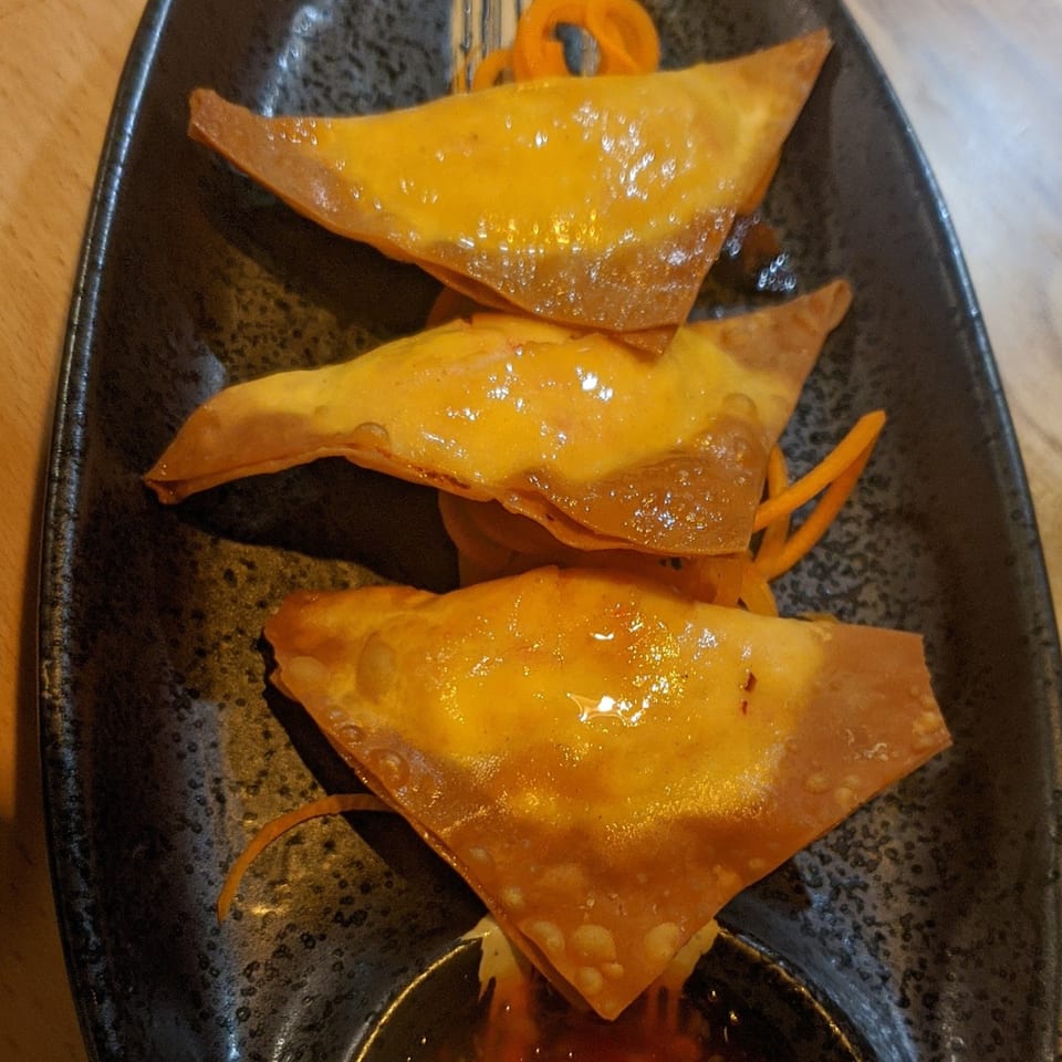 Three golden-brown fried wontons with a glossy glaze, garnished with shredded carrots on a dark plate.
